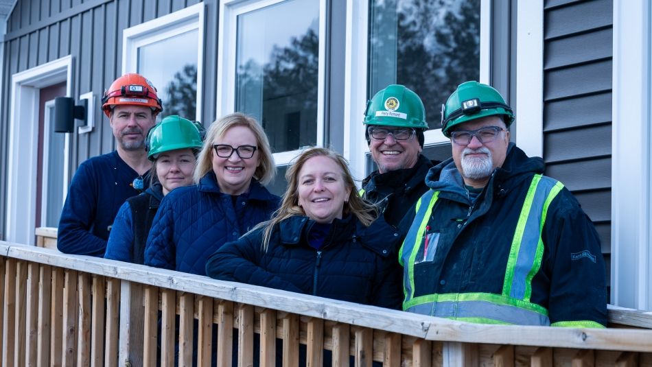 Unifor leaders and members wearing hardhats in front of modular house.