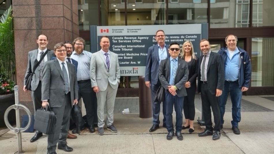 Un groupe de personnes se tient devant un panneau de l'Agence du revenu du Canada dans la rue.