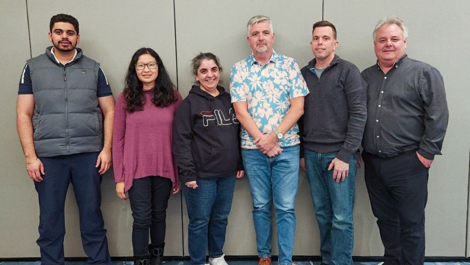 “Six people standing near a wall posing for a photo.”