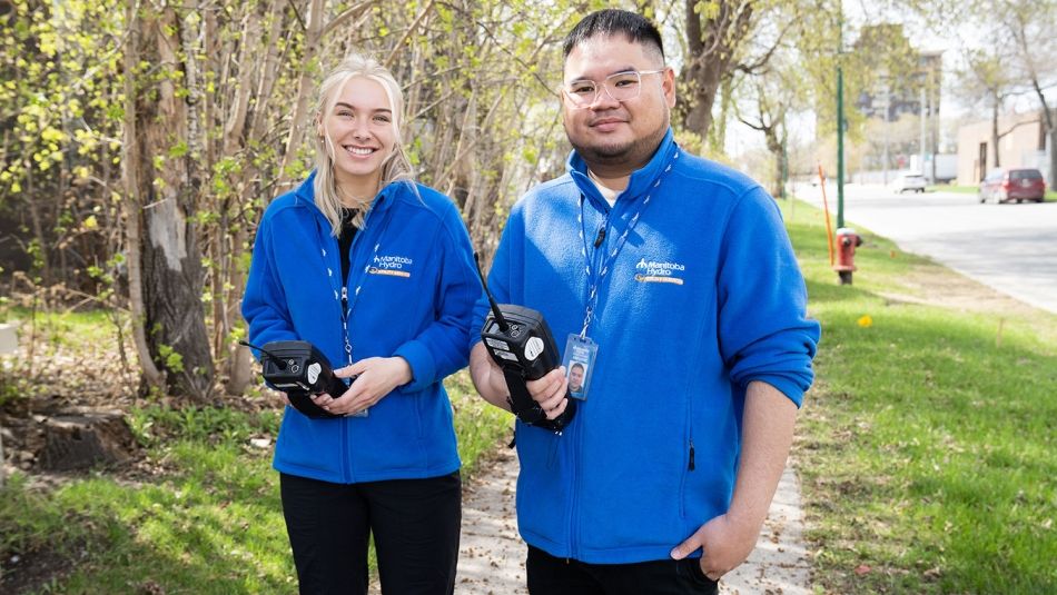 Deux membres d'Unifor portant des vestes bleues à l'extérieur et tenant des appareils électroniques.