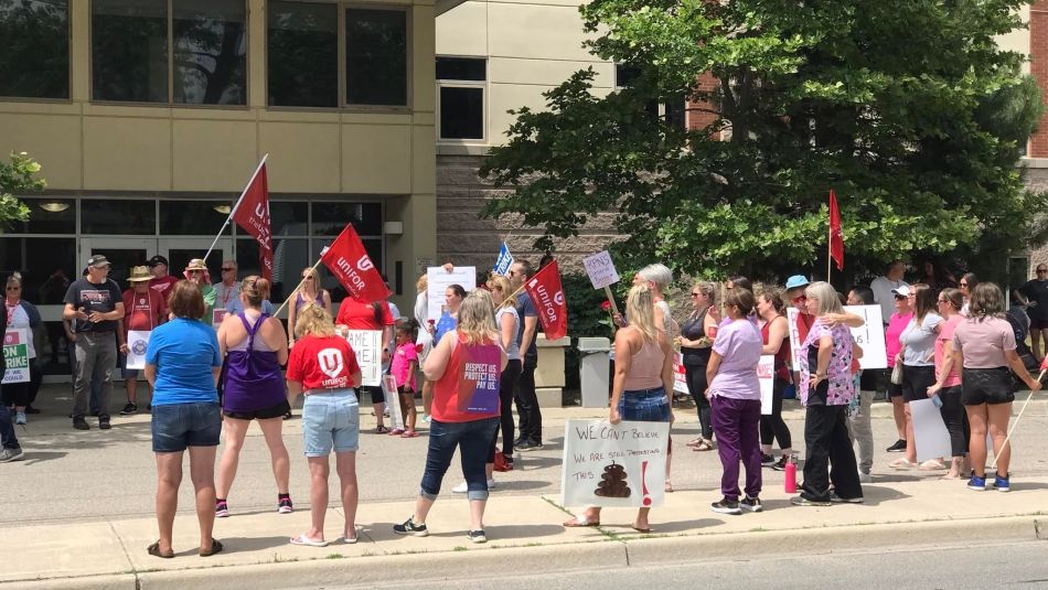 Unifor members from Riverview Gardens in Chatham, Ontario line the side of a road holding picket signs.