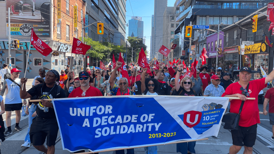 A group of people marching with a Unifor banner.