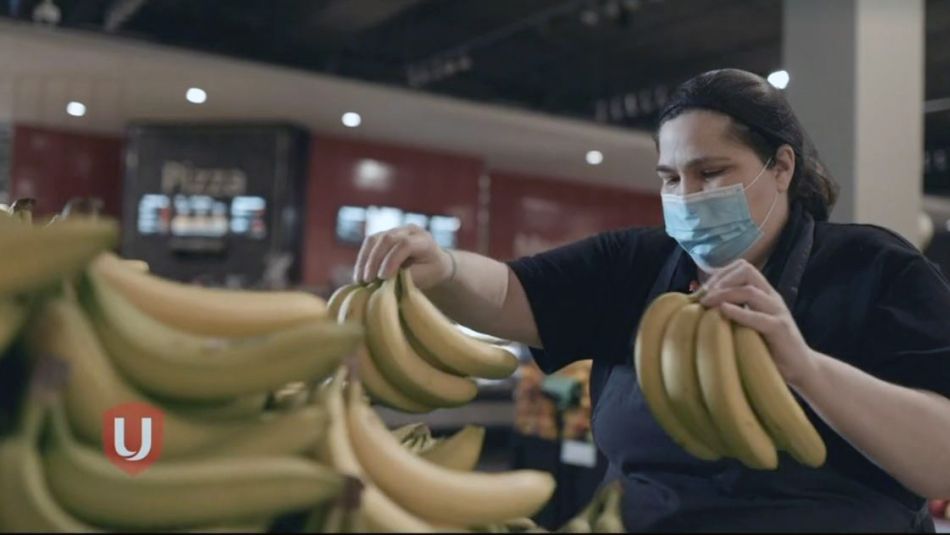 Une employée d'épicerie portant un masque trie des bananes.