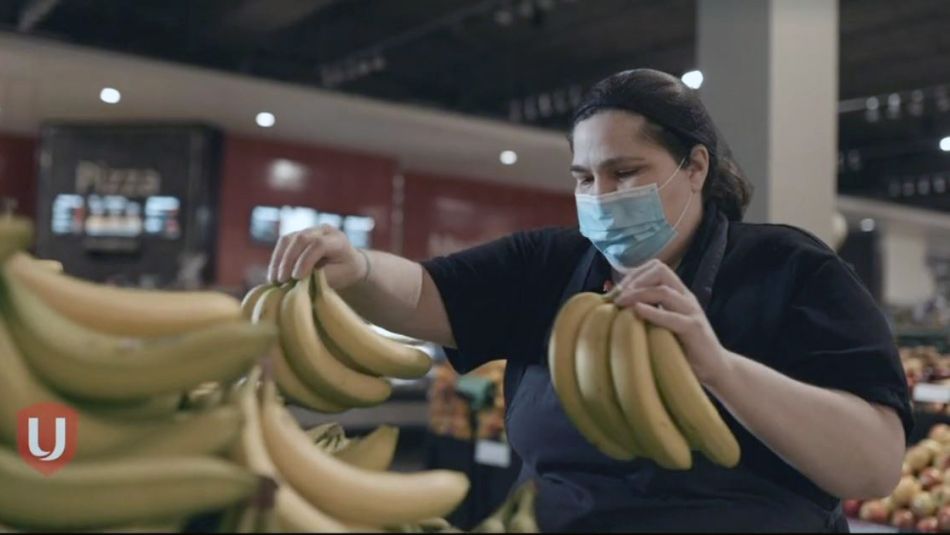 Une employée d'épicerie portant un masque trie des bananes.
