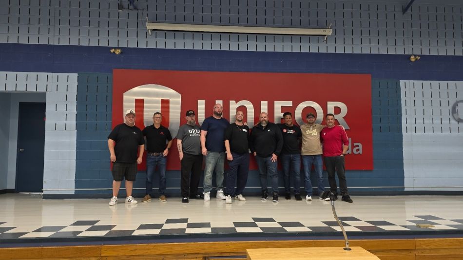 A group of men posing in front of a Unifor sign