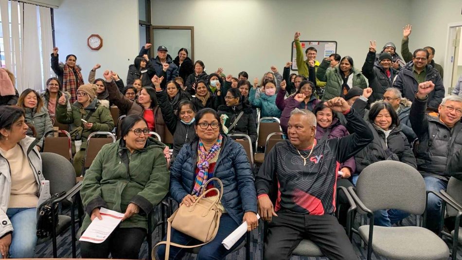 A large group of people sitting in chairs a few have their fists in the air.