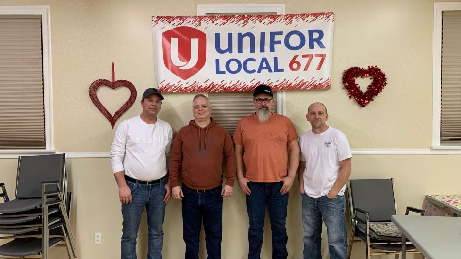 Four men, local and national union representatives, pose in front of a Local 677 banner. 