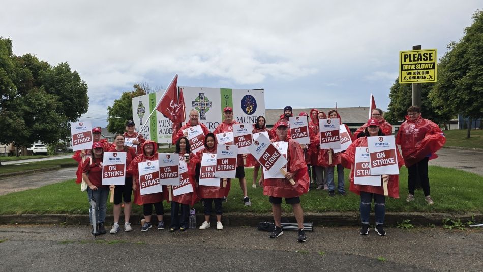 Unifor members at Munro Academy wearing rain ponchos and holding strike signs and Unifor flags.