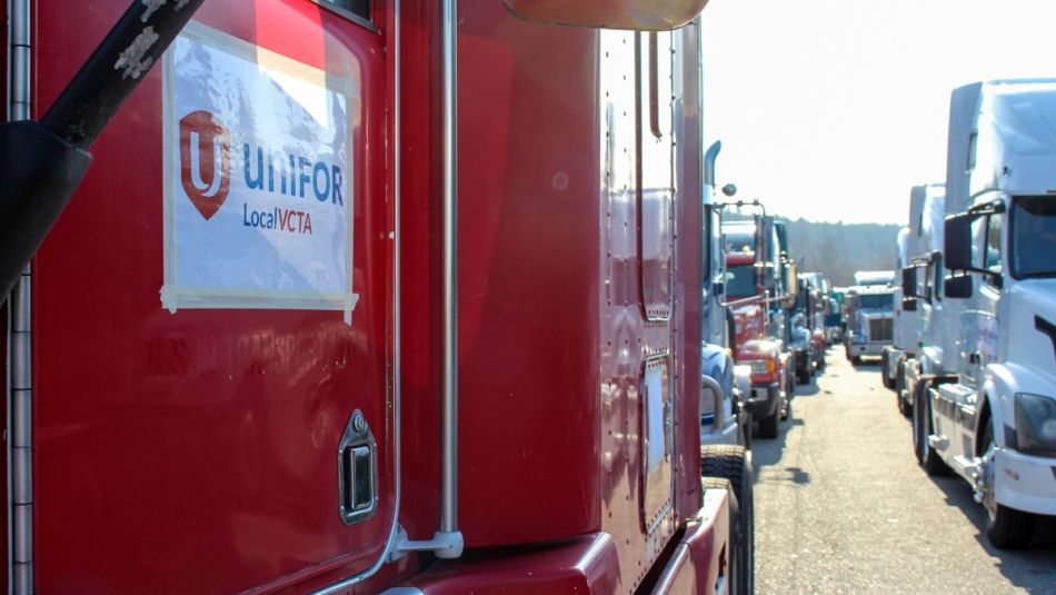 “Two long lines of trucks. A Unifor sign is visible taped to a truck door in the foreground.”