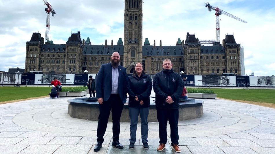 hannon Sampson, présidente de la section locale 1-MWF d'Unifor, se tient entre Adam Slaunwhite, agent d'affaires de la section locale 1-MWF, et Adam Hersey, représentant national d'Unifor, devant la Colline du Parlement à Ottawa.
