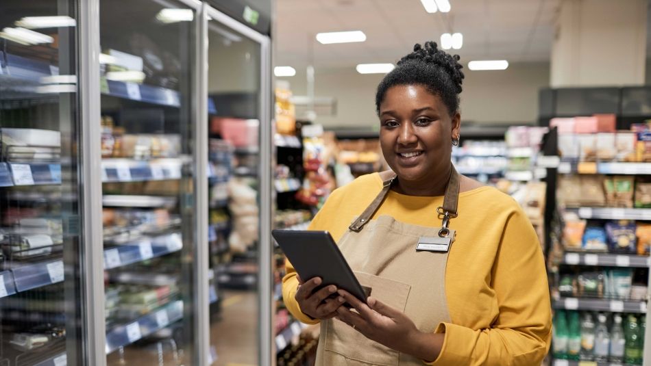 A black women holding looking at a tablet in a grocery isle