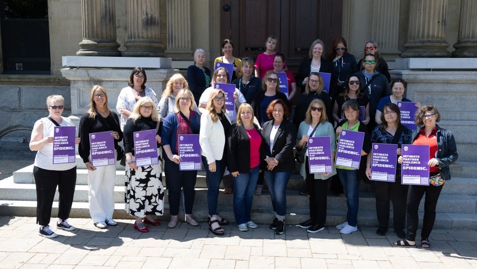 A large group of women posing outdoors holding IPV placards