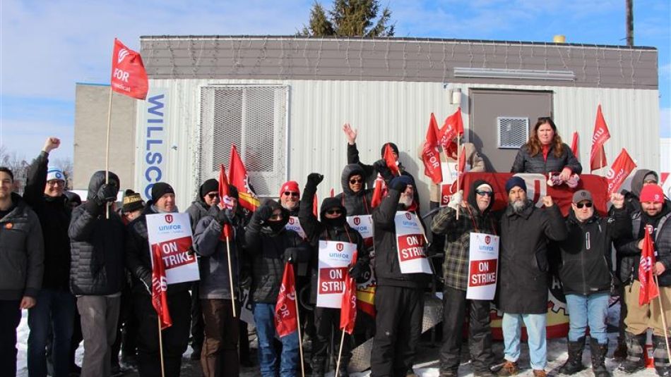 A large group holding Unifor flags and placard that read "on strike"