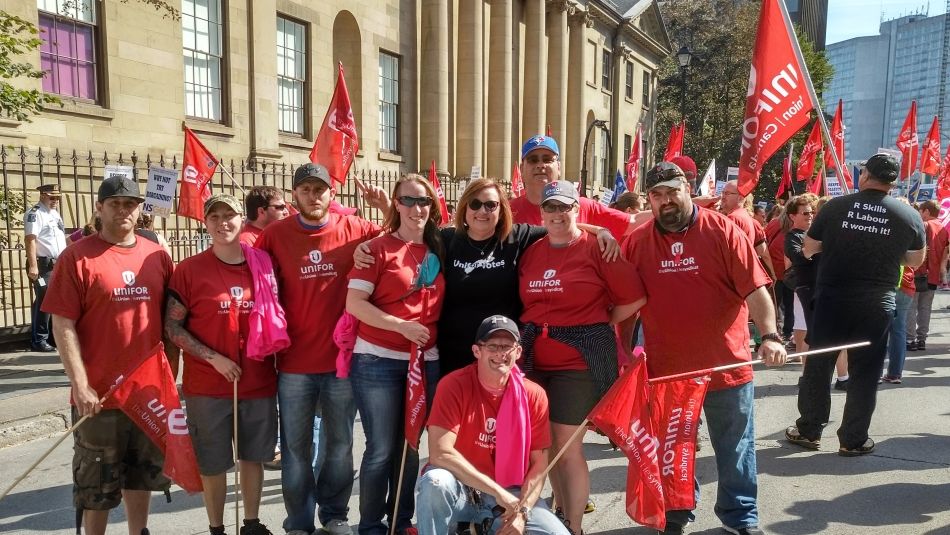 A large group outside wearing red Unifor shirts and holding Unifor flags