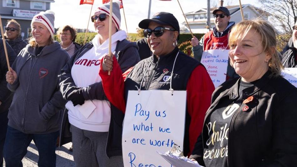 A group of women outside holding placcards and flags on a fall day.