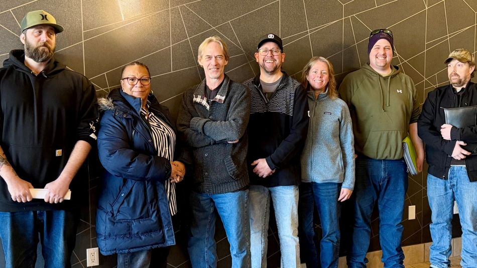 Seven people standing in front of a gray wall with geo shapes