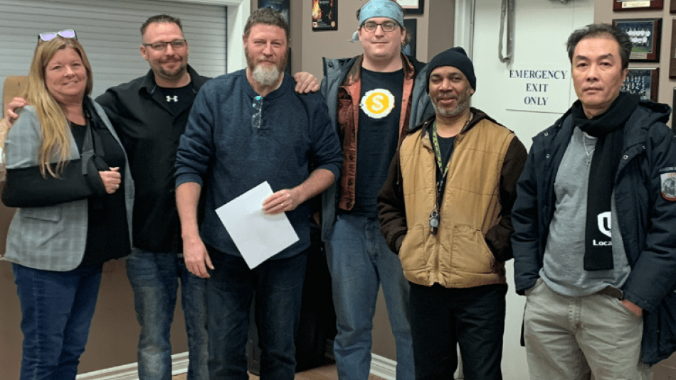 A group of people standing in front of an exit door. A man in the middle holds a sheet of paper.