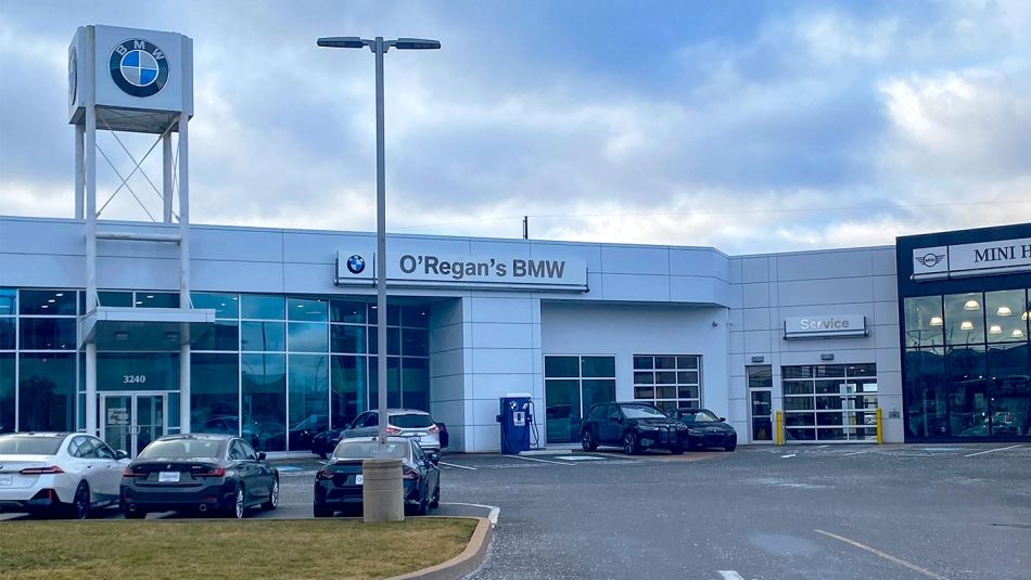 An exterior view of O'Regan's BMW dealership showing several cars parked out front and the service bay doors.