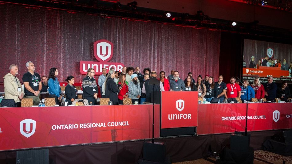 Unifor delegates stand on stage behind a podium during the Ontario Regional Council meeting