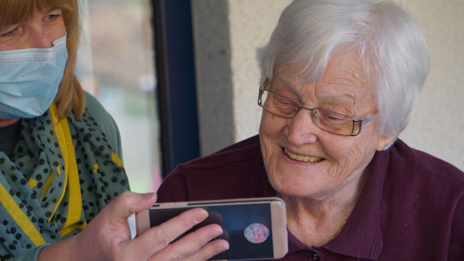 Worker wearing mask shows grey haired woman an iphone