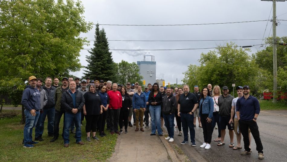 A large group outdoors in front of trees and a mill in the background