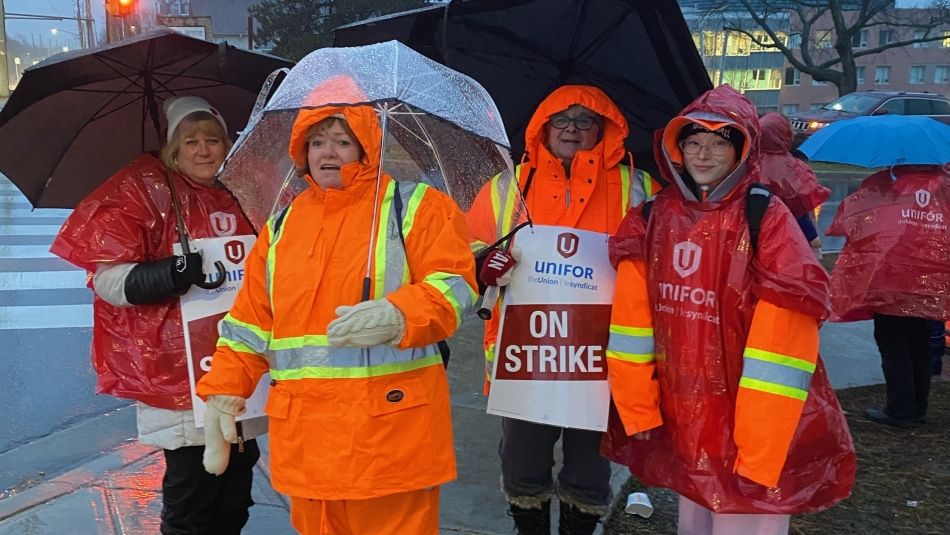 Striking Durham College Foodservice wearing rain gear and umbrellas on the picketline.