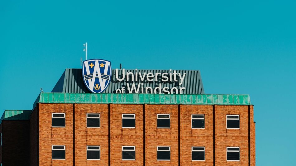 Brown building with University of Windsor sign in the background and turquoise sky.