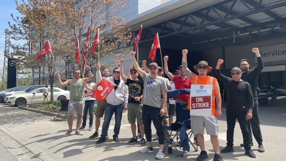 Members outside at Mercedes-Benz dealership in midtown Toronto wave Unifor flags and their fits in the air on a sunny day.