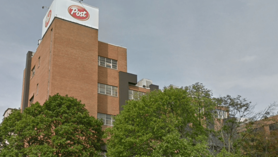 Brown factory building with “Post” logo in white and red with green trees in the foreground.