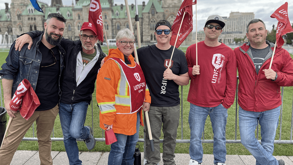 ”Six people with Unifor flags posing on Parliament Hill”