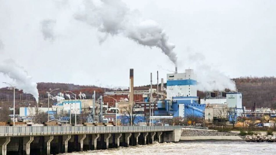 RYAM Temiscaming Wide scene of a factory with smoke plume from smokestack and river with bridge in the foreground.