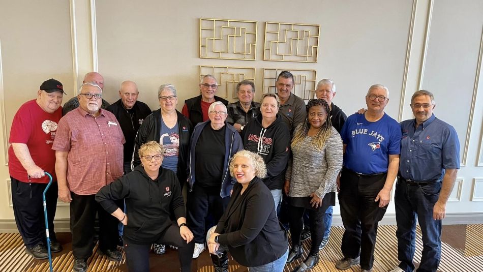 A group of people, some kneeling, others standing, in front of four gold mosaic artwork pieces.