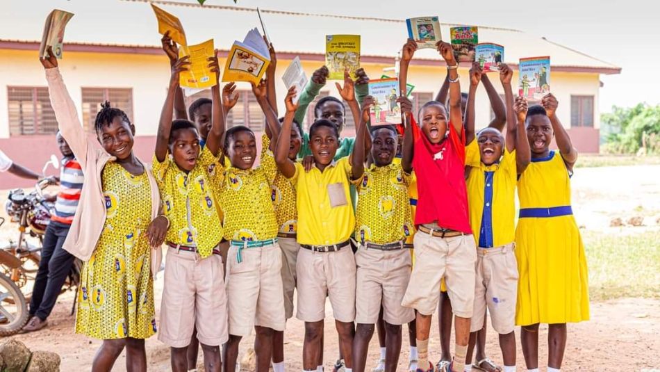 A group of kids holding up books over their heads all are wearing white shorts and yellow tops