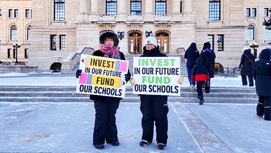 Deux personnes devant le bâtiment de la législature de la Saskatchewan tiennent des pancartes faites à la main sur lesquelles on peut lire "Investissez dans notre avenir, financez nos écoles".