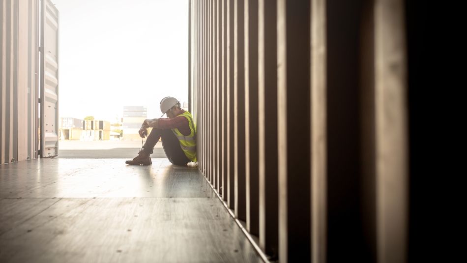 Sad worker sitting with head down and arms wrapped around knees