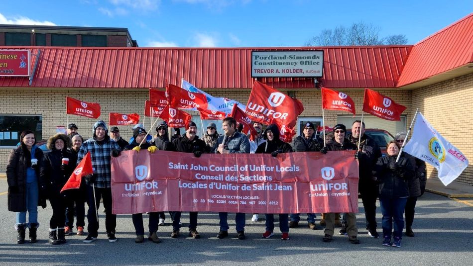Des membres d'Unifor aggisant des drapeau et tennant une banière lors d'un rassemblement.