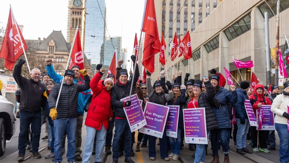 A large crowd holding red Unifor flags and placcards.