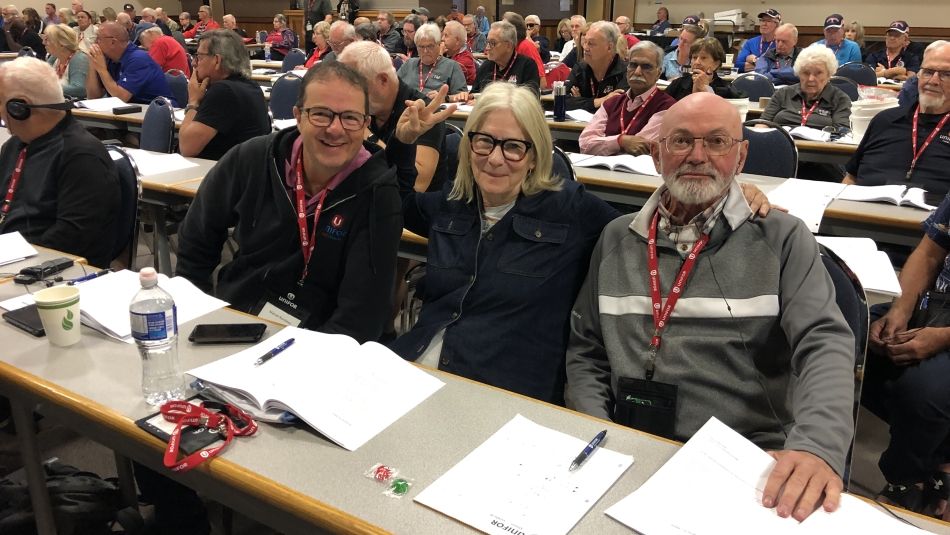 Three people sitting at a table with people at a conference around them.