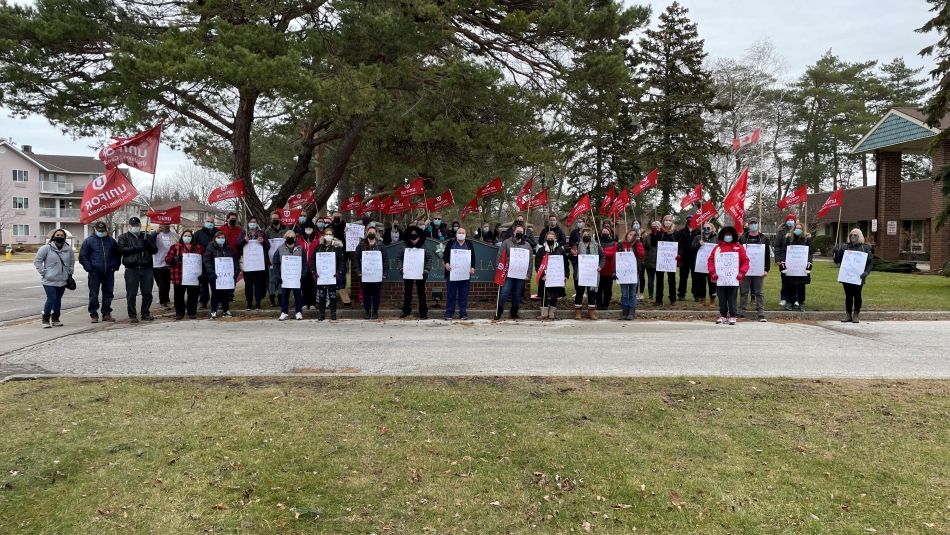 Large group of long-term care workers stand holding placards and flags