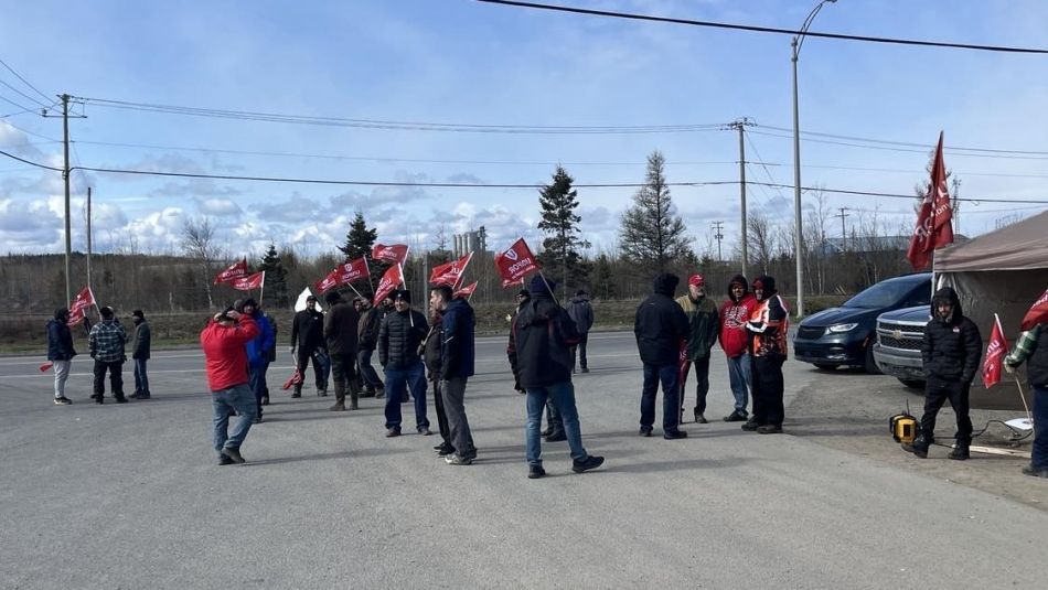 A group of people carrying red Unifor flags, marching on the picket line.