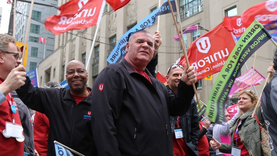 Scott Batemen at a rally holding up a red Unifor flag.