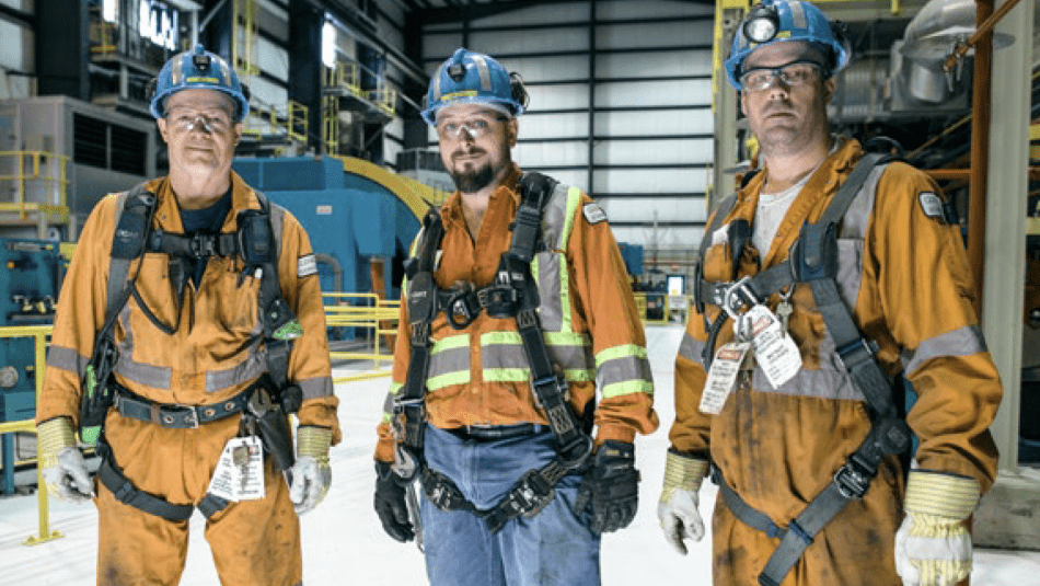 Three workers wearing coveralls in plant.