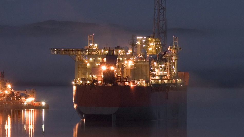 Large ship with many lights on calm water at night. Part of a smaller ship can be seen beside it. 