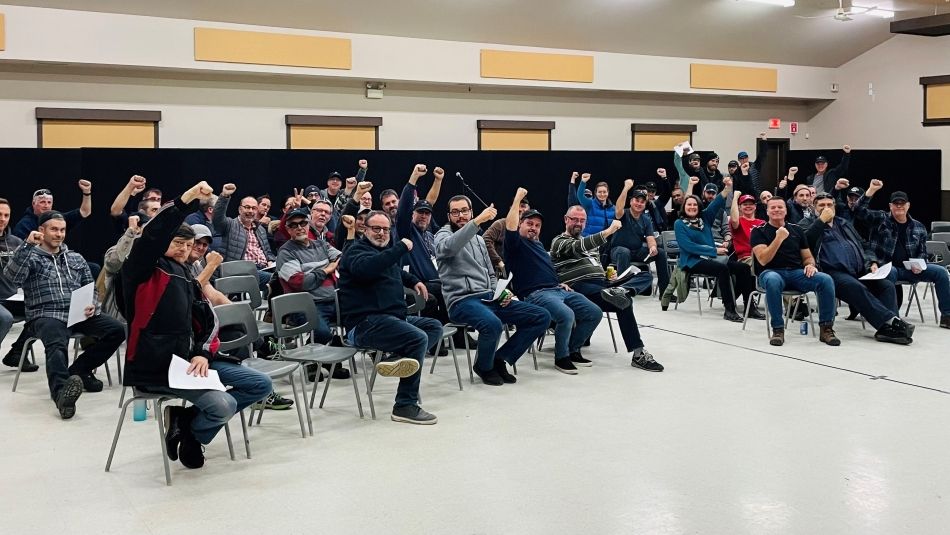 A large group of people sit in a room with fists raised as a show of strength