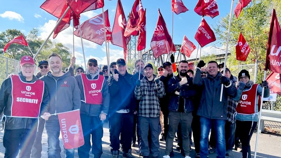 Un groupe de membres d'Unifor employés à la Corporation de gestion de la Voie maritime du Saint-Laurent tiennent des drapeaux sur un piquet de grève.