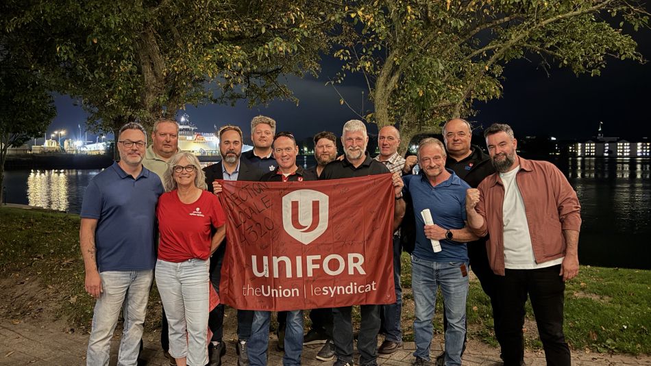 A large group at night holding up a red Unifor flag