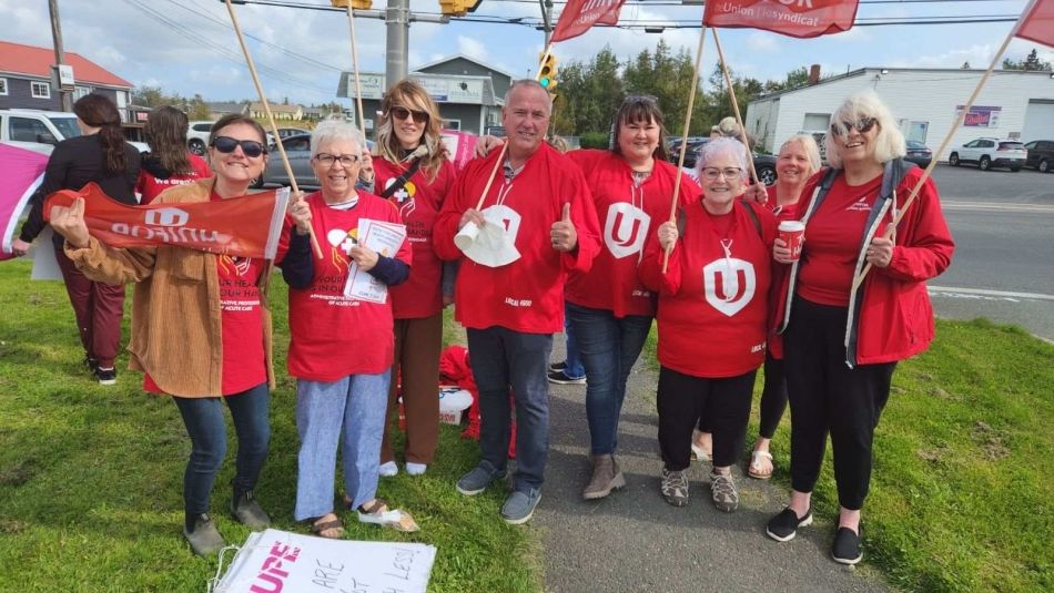 A group of Unifor members wearing red and holding flags stand outside a hospital in Cape Breton.