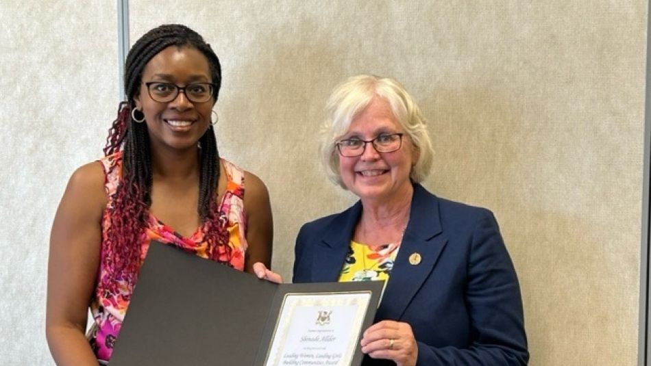 Two women stand together, holding a certificate award.