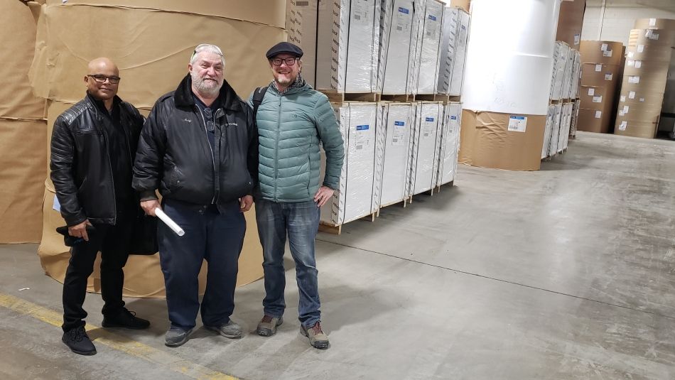 Three men standing together with warehouse materials in the background.