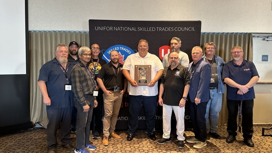A man stands in the middle of a group photo holding an award